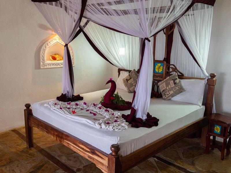 Cama con estructura de madera y mosquitera blanca decorada en una habitación de hotel.