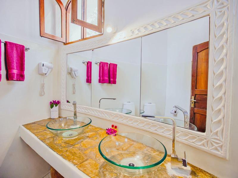 Baño del hotel con dos lavabos de vidrio, espejo grande, toallas rosas y encimera amarilla.