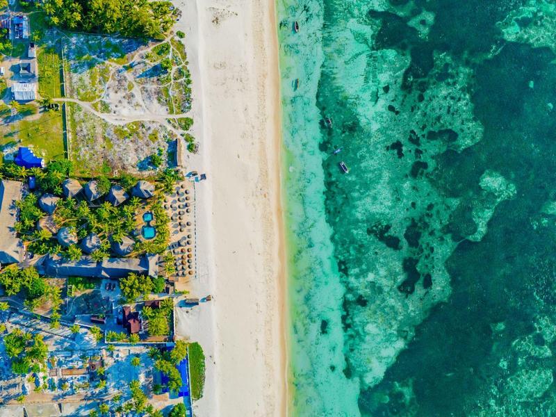 Vista aérea de una playa de arena amplia con agua turquesa clara junto a un asentamiento costero.