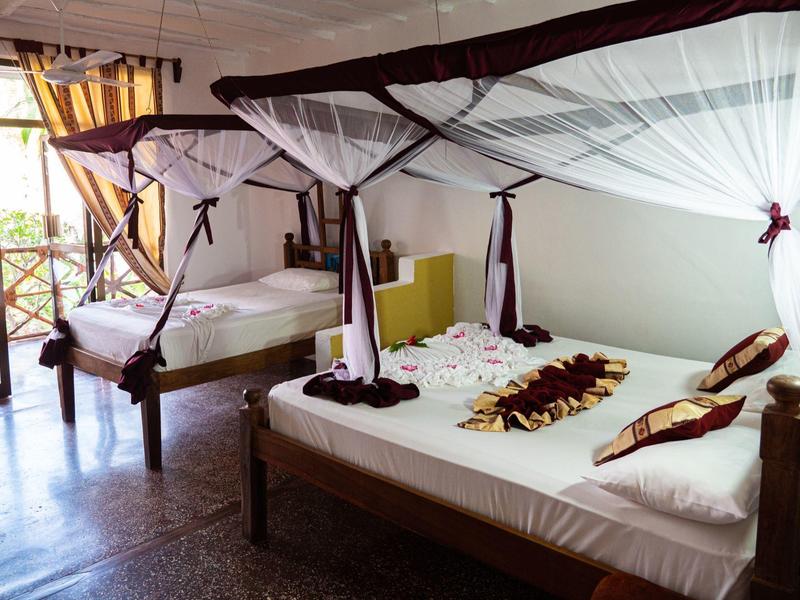 Habitación luminosa con dos camas con dosel, decoración con pétalos y muebles de madera.