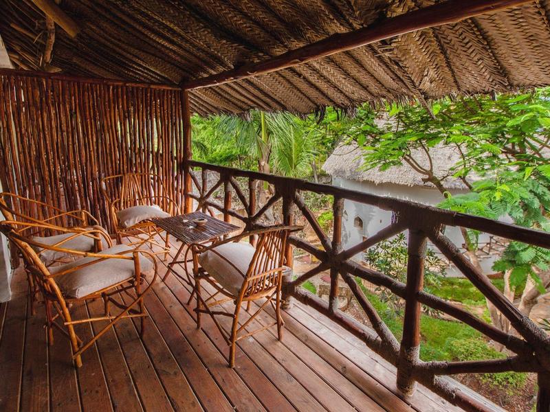 Balcón acogedor de madera con sillas y mesa de bambú, rodeado de follaje verde.
