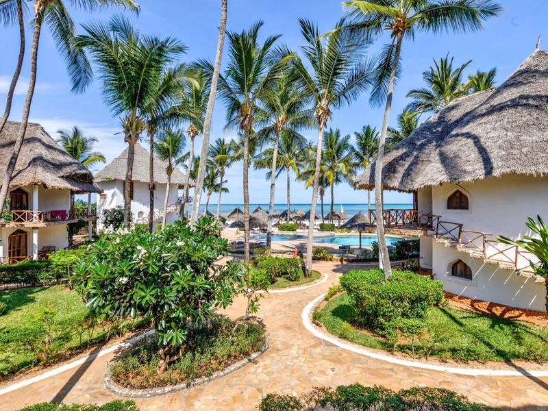 Resort tropical con bungalows redondos, palmeras y vista al mar bajo cielo azul.