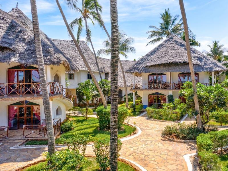 Complejo hotelero con bungalows de techo de paja, palmeras y caminos bien cuidados bajo el sol.