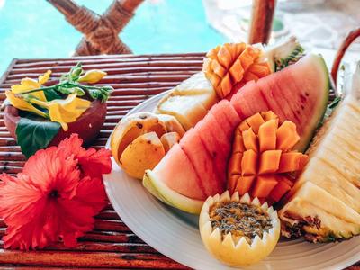 Ein Teller mit verschiedenen geschnittenen tropischen Früchten und einer roten Blume auf einem Holztisch.