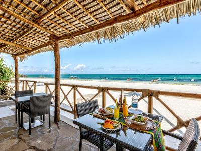 Terrasse mit gedecktem Tisch und Blick auf einen weißen Sandstrand und das blaue Meer.