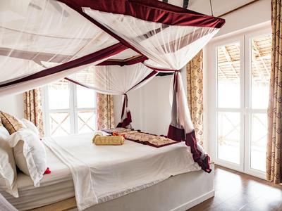 Elegantes Doppelbett mit Baldachin und weißen sowie bordeauxroten Vorhängen in hellem Zimmer mit Balkon.