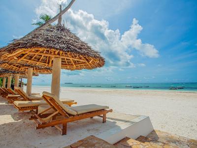Reihen von Holzliegen mit Strohdächern am weißen Sandstrand unter blauem Himmel.