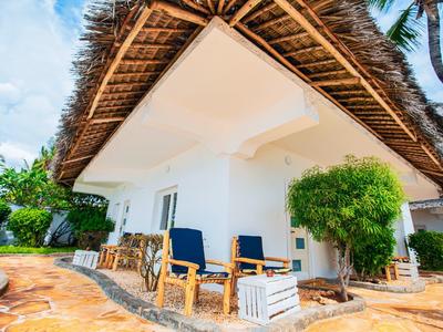 Außenbereich einer Unterkunft mit Holzstühlen und üppiger Vegetation unter einem Strohdach.