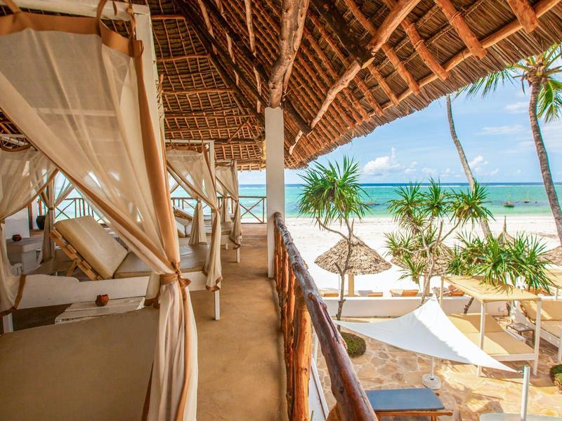 Offener Strandbungalow mit hölzernen Betten und Blick auf den Meerblick und Palmen.