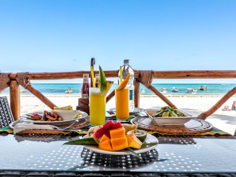 Tisch mit Frühstück, Obst und Säften am Strand mit Blick auf das Meer.