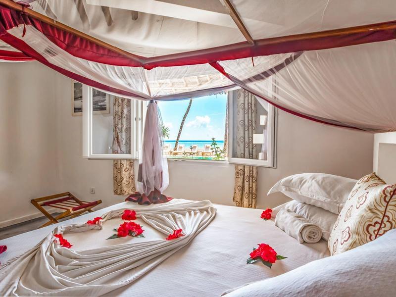 Elegantes Hotelzimmer mit Himmelbett, blumenverziert und Meerblick durch das Fenster.