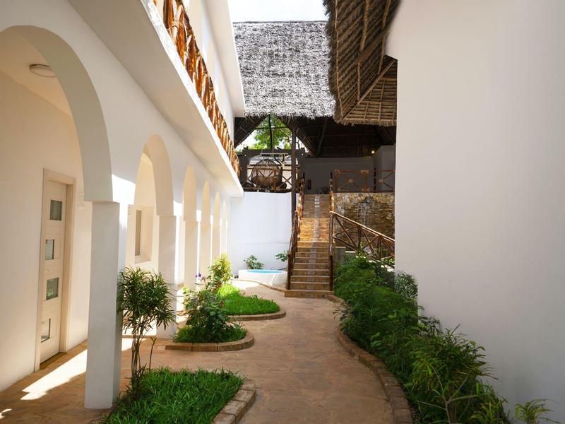 Innenhof mit weiß gestrichenen Wänden, Bögen, Pflanzen und einem schmalen gepflasterten Weg.
