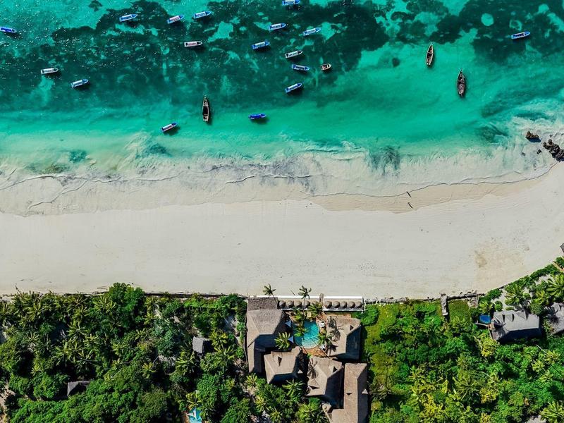 Luftaufnahme eines tropischen Strandresorts mit türkisfarbenem Wasser und feinem Sand.