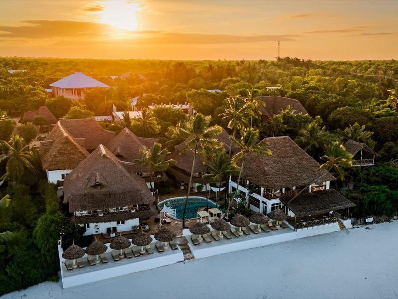 Resort mit Strohdachbungalows und Pool am weißen Sandstrand bei Sonnenuntergang