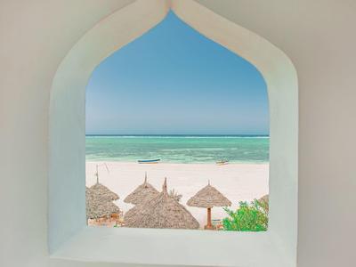 Blick durch ein weißes Fenster auf einen Strand mit Strohdächern und türkisfarbenem Meer