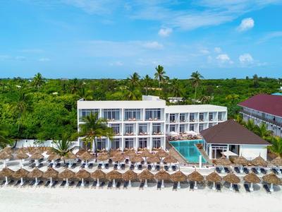 Hotel con piscina e molte sdraio su spiaggia di sabbia bianca sotto cielo azzurro.