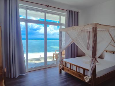 Camera d'hotel luminosa con letto a baldacchino e ampia finestra con vista mare.