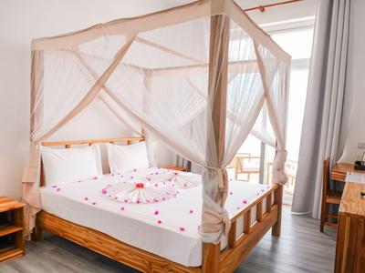 Camera d'albergo luminosa con letto a baldacchino, biancheria bianca e porta del balcone con luce diurna.