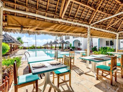 Terrazza soleggiata con tavoli e sedie accanto a una piscina e edifici bianchi.