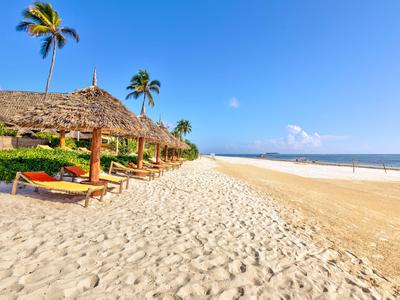 Spiaggia con sabbia, palme e sdraio sotto tetti di paglia vicino al mare sotto un cielo limpido.