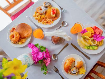 Vier Teller mit verschiedenen Frühstücksoptionen und Orangensaft auf einem weißen Tisch mit Blumen.