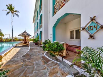 Außenbereich eines Hotels mit Pool, Steinweg, Palmen und Veranda mit Sitzbereich.