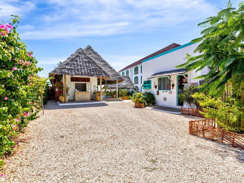 Innenhof mit Kiesweg, üppiger Bepflanzung und mehreren Gebäuden unter blauem Himmel.