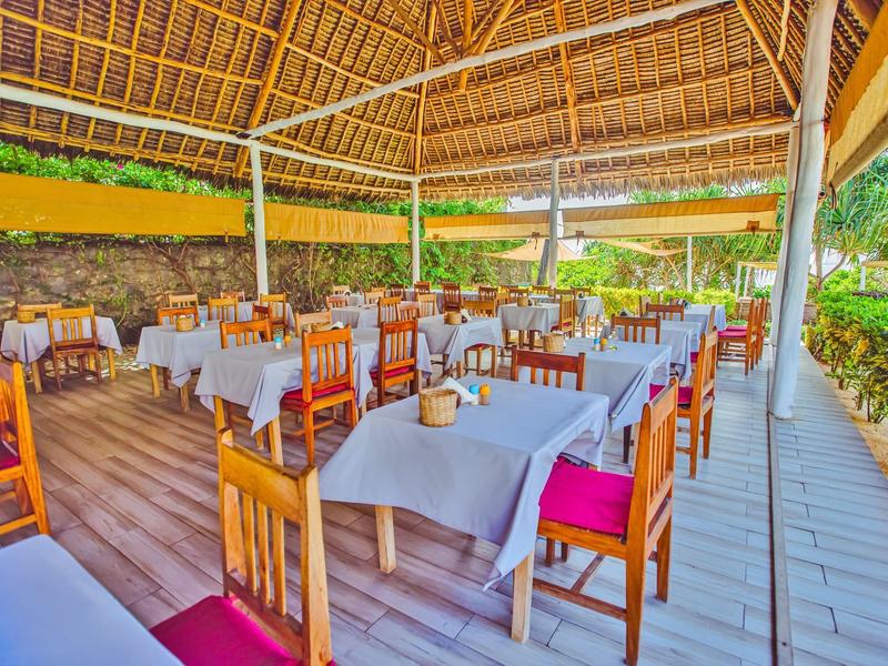 Überdachter Außenbereich eines Restaurants mit Holzböden, Holzmöbeln und weißen Tischtüchern.