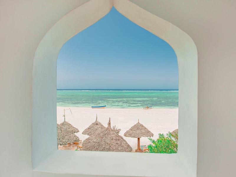 Blick durch ein weißes Fenster auf einen Strand mit Strohdächern und türkisfarbenem Meer