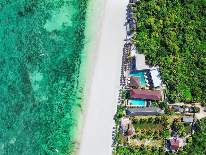 Luftaufnahme eines Resorts mit weißem Sandstrand und klarem türkisem Wasser neben dichtem Grün.