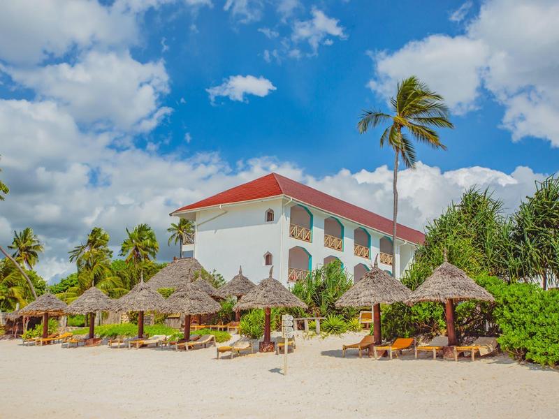 Hotelgebäude mit rotem Dach am Sandstrand, Palmen und Sonnenschirmen aus Stroh