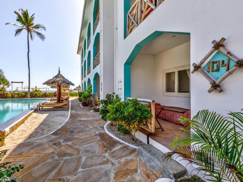 Außenbereich eines Hotels mit Pool, Steinweg, Palmen und Veranda mit Sitzbereich.