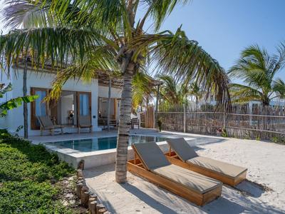 Zwei Sonnenliegen am Pool einer Villa mit Palmen und klarem Himmel im Hintergrund.