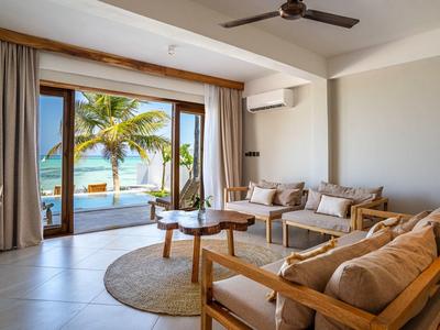 Modernes Wohnzimmer mit Sitzgruppe und Blick auf tropische Strandlandschaft durch große Schiebetüren.