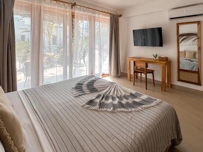 Modernes Hotelzimmer mit Doppelbett, Schreibtisch, Fernseher und großem Fenster mit Vorhängen.