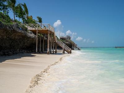 Sandstrand mit klarem türkisfarbenem Wasser und Treppe zu einer Holzterrasse am Fels