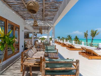Hölzerne und gepolsterte Sitzgelegenheiten auf einer Terrasse mit Blick auf den Strand und das Meer bei klarem Himmel.