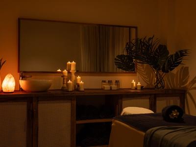 Dunkler Wellnessraum mit massagetisch, Kerzenlicht und Dekoration für Entspannung.