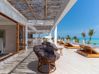 Terrasse mit Korbsesseln und Liegestühlen neben einem Fitnessraum mit Blick auf das Meer.