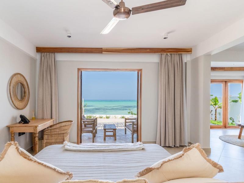 Helles Hotelzimmer mit Blick auf Terrasse und Meer, modern eingerichtet mit hellen Farben.