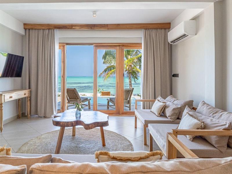 Helle Hotelzimmer mit Holzmöbeln, Sofa, Tisch und Balkon mit Meerblick.
