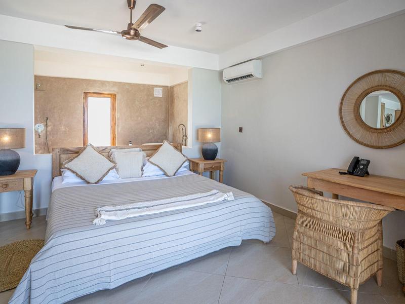 Helles Schlafzimmer mit Doppelbett, zwei Nachttischen, einem Schreibtisch und einem Ventilator an der Decke.