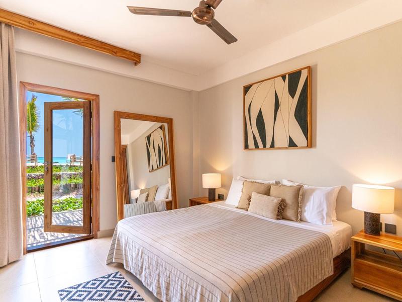 Gemütliches Schlafzimmer mit Doppelbett, zwei Nachttischen, Fenster mit Vorhängen und Deckenventilator.