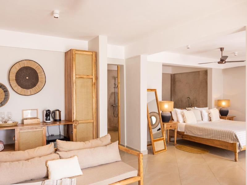 Modern eingerichtetes Hotelzimmer mit Sofa, Doppelbett und dekorativen Wandobjekten in warmen Farben.