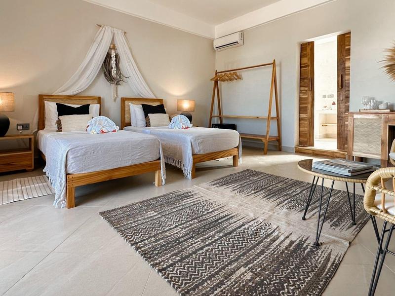 Helles Hotelzimmer mit zwei Einzelbetten, modernem Mobiliar und Teppichboden.