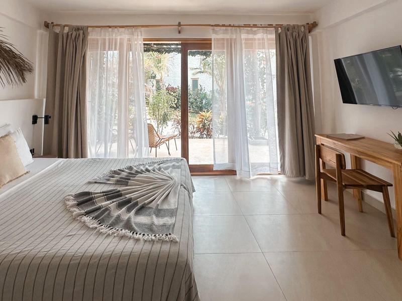 Modernes Schlafzimmer mit großem Bett, Holzmöbeln und Zugang zu einer Terrasse mit Pflanzen.