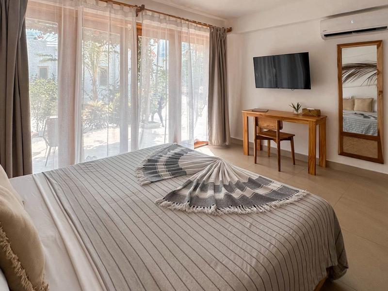 Modernes Hotelzimmer mit Doppelbett, Schreibtisch, Fernseher und großem Fenster mit Vorhängen.