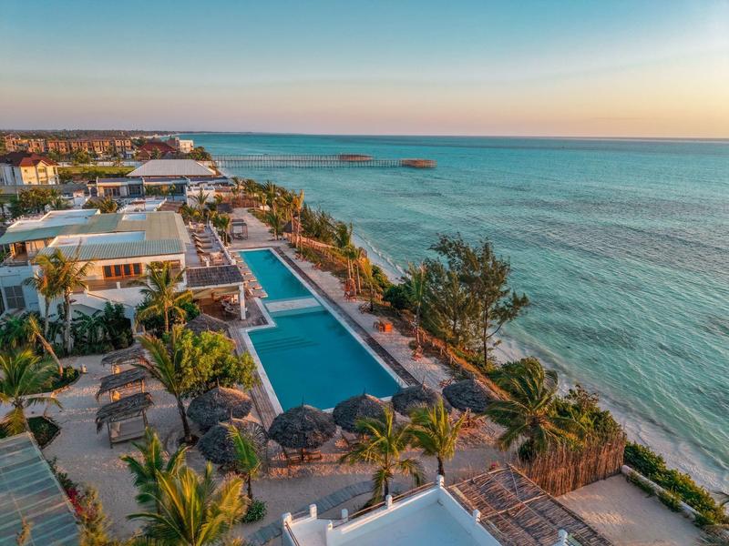 Moderner Hotelkomplex mit Pool und tropischen Pflanzen an der Küste bei Sonnenuntergang