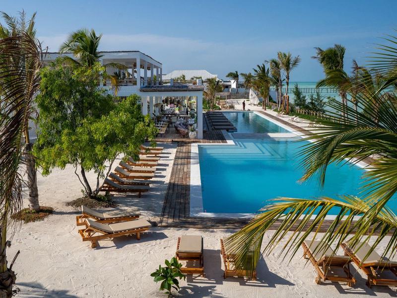 Moderner Hotelpool mit Liegestühlen und Palmen in sonniger Umgebung.