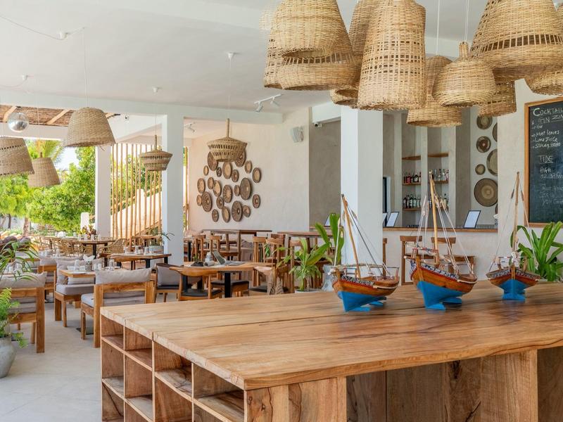 Hell eingerichtetes Café mit Holzmöbeln, Korblampen und Blick auf einen grünen Außenbereich.